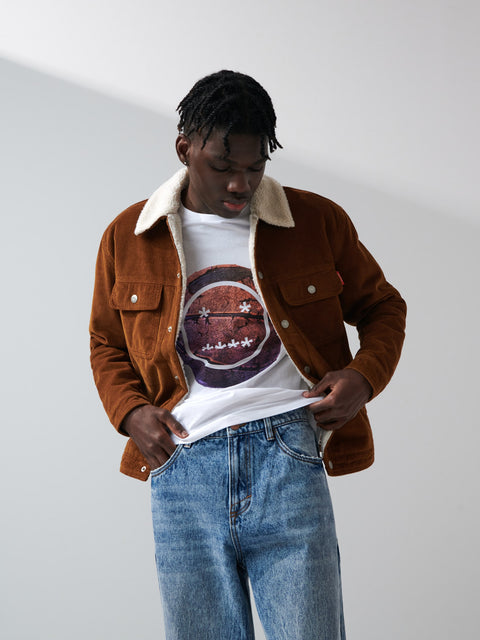 Person wearing a brown jacket with a white shirt and blue jeans on a plain background
