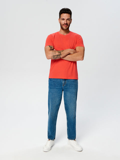 Man wearing a red t-shirt and blue jeans standing against a white background