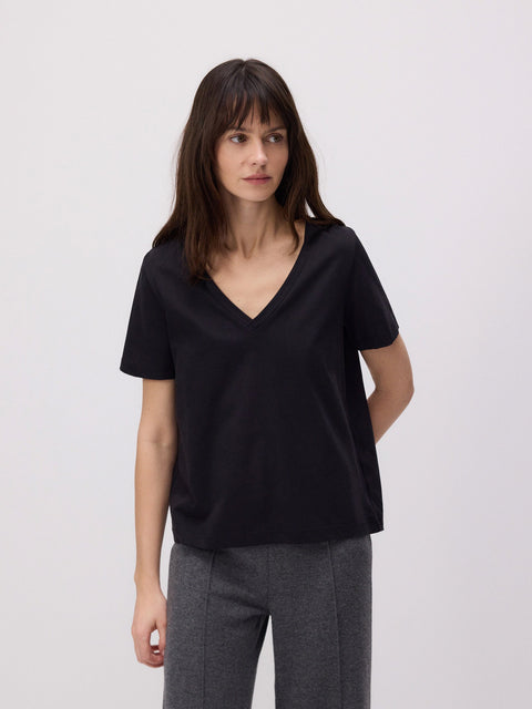 Woman wearing a black top and gray pants against a plain background
