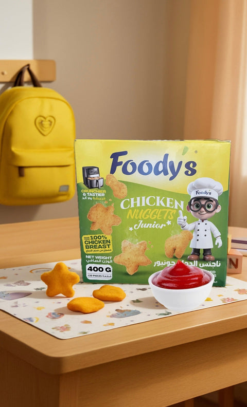Foody's Chicken Nuggets Junior packaging on a table with snacks and a yellow backpack in the background.