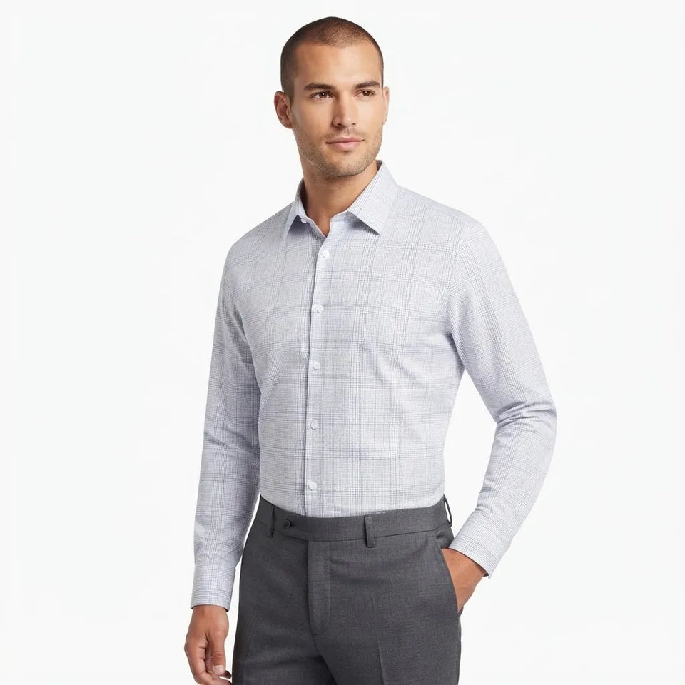 A man wearing a light gray and white micro-check patterned long-sleeve dress shirt with dark gray trousers, standing against a plain white studio background.