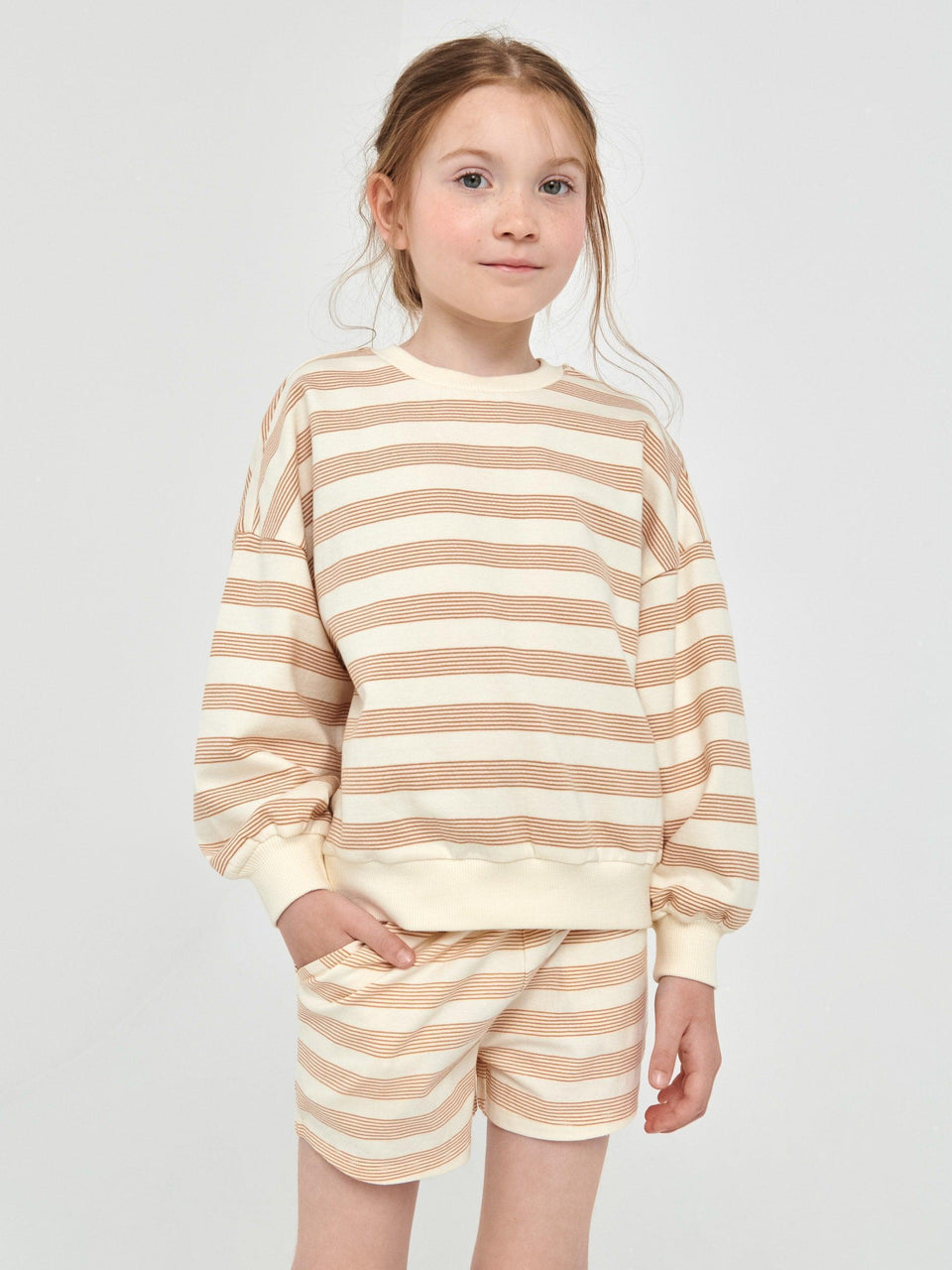 Young girl wearing a beige and white striped outfit on a light gray background