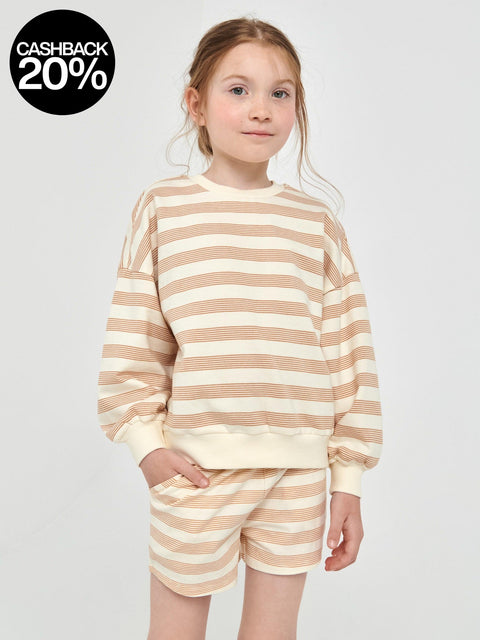 Young girl wearing a beige and white striped outfit on a light gray background