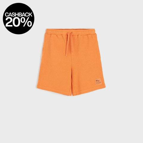 Orange shorts with a brand logo on a light gray background