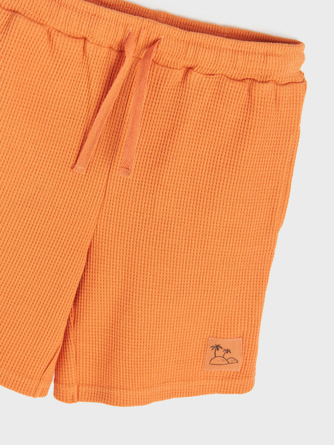 Orange shorts with a small logo on a light gray background