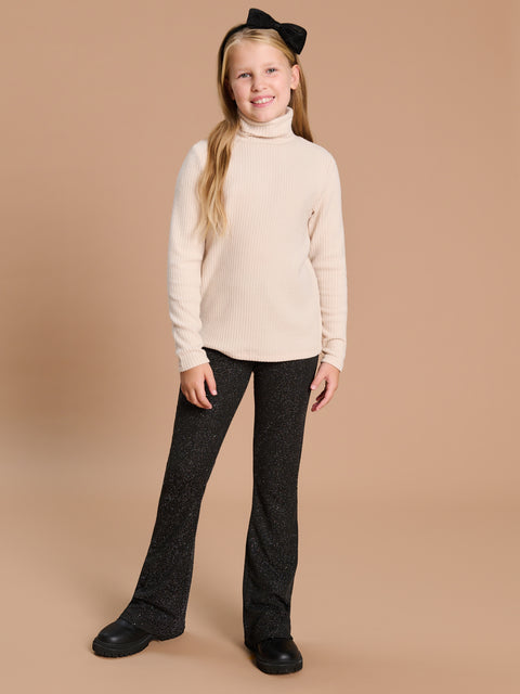 Young girl wearing a cream sweater and black pants on a beige background