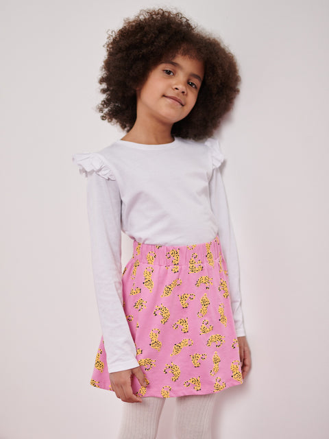 Young girl wearing a light gray top and pink skirt with yellow patterns on a plain background