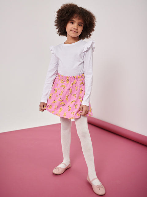 Young girl wearing a white shirt, pink skirt with yellow pattern, and white tights on a pink and white background.