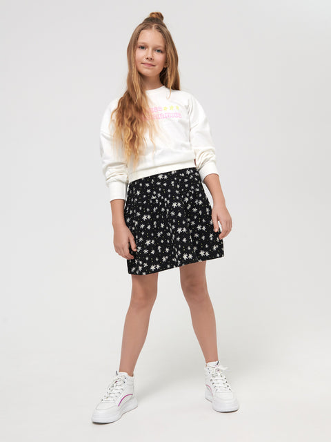 Young girl wearing a white sweatshirt with text and a black star-patterned skirt on a white background