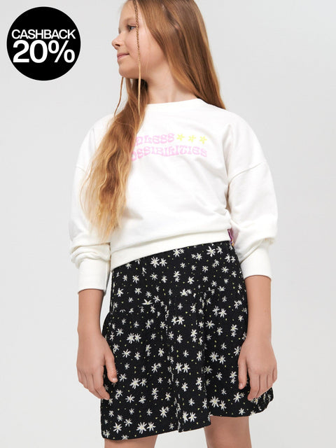 Young girl wearing a white sweatshirt with colorful text and a black star-patterned skirt on a light gray background