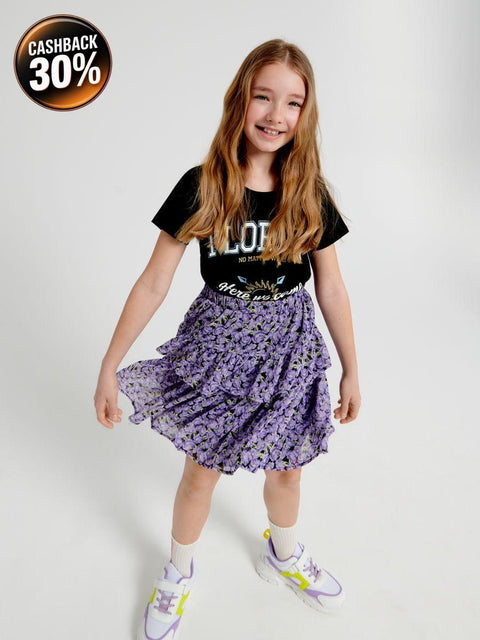 Young girl wearing a black t-shirt with text and a purple floral skirt on a white background