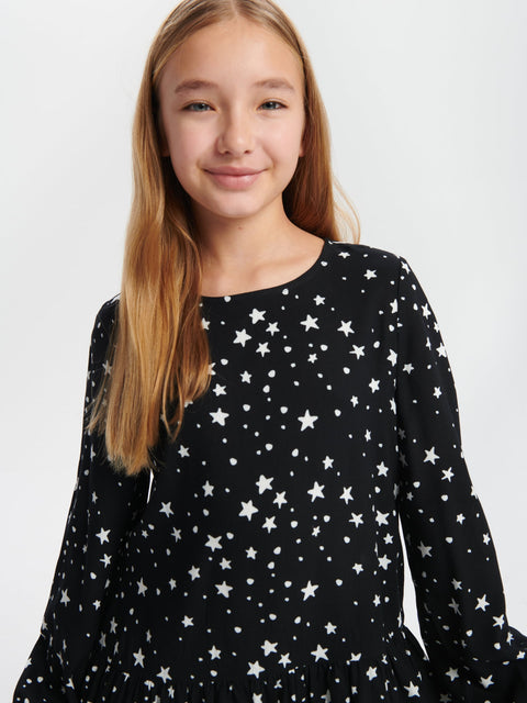Young girl wearing a black dress with white star pattern against a plain background