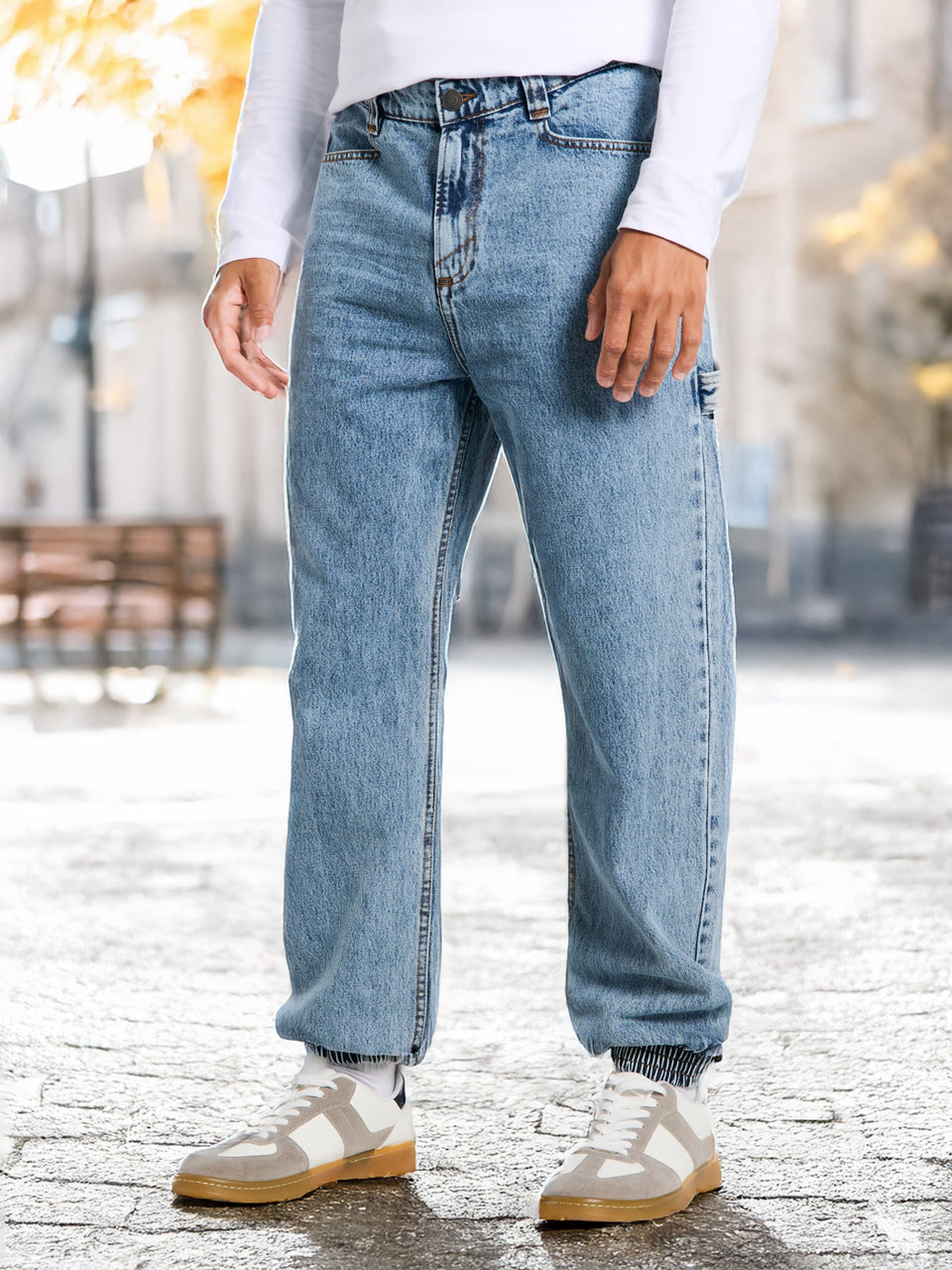 Person wearing light blue jeans and white sneakers on a blurred outdoor background