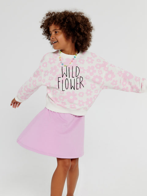 Child wearing a pink floral sweatshirt with 'Wild Flower' text and a pink skirt on a white background