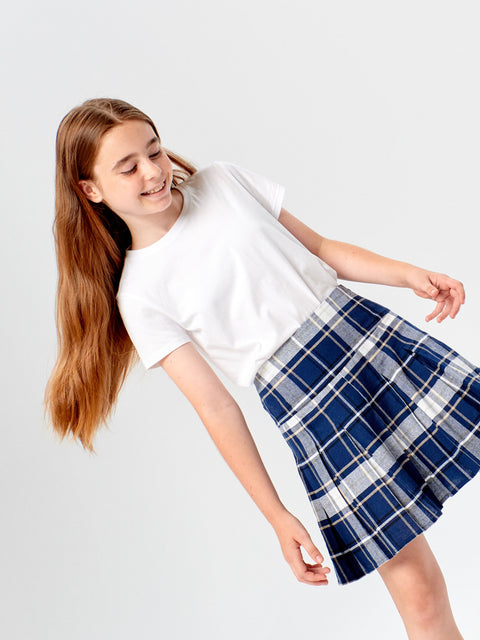Young girl wearing a white t-shirt and blue plaid skirt on a light gray background