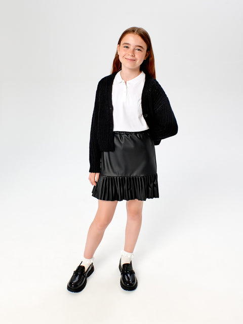 Young girl wearing a black cardigan, white shirt, and black pleated skirt on a white background