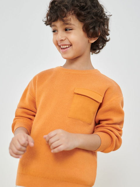 Child wearing an orange sweater on a plain background
