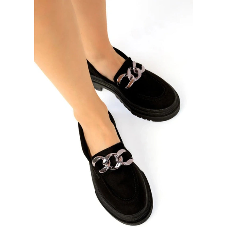 Black suede loafers with chunky black platform soles and a prominent silver-tone chain detail across the vamp, shown on a model's feet against a white background.