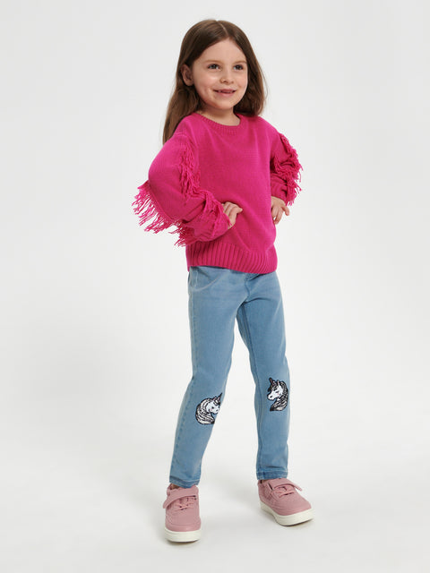 Young girl wearing a pink sweater and blue jeans with patches on a white background