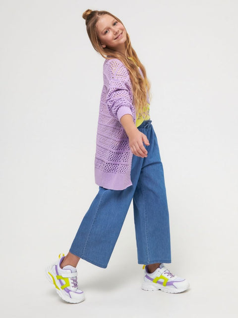 Young girl wearing a purple sweater, blue jeans, and colorful sneakers on a white background