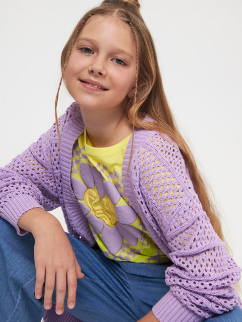 Young girl wearing a purple knitted cardigan over a colorful shirt on a white background