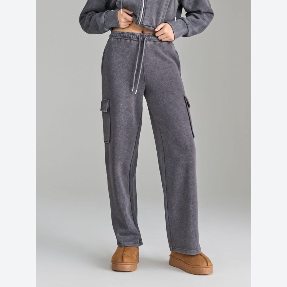 A person wearing gray drawstring sweatpants with side cargo pockets, paired with a matching gray cropped top and tan platform shoes, photographed against a light gray studio background.