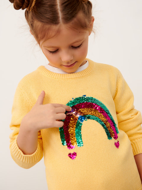 Child wearing a yellow sweater with a colorful rainbow sequin design on a plain background