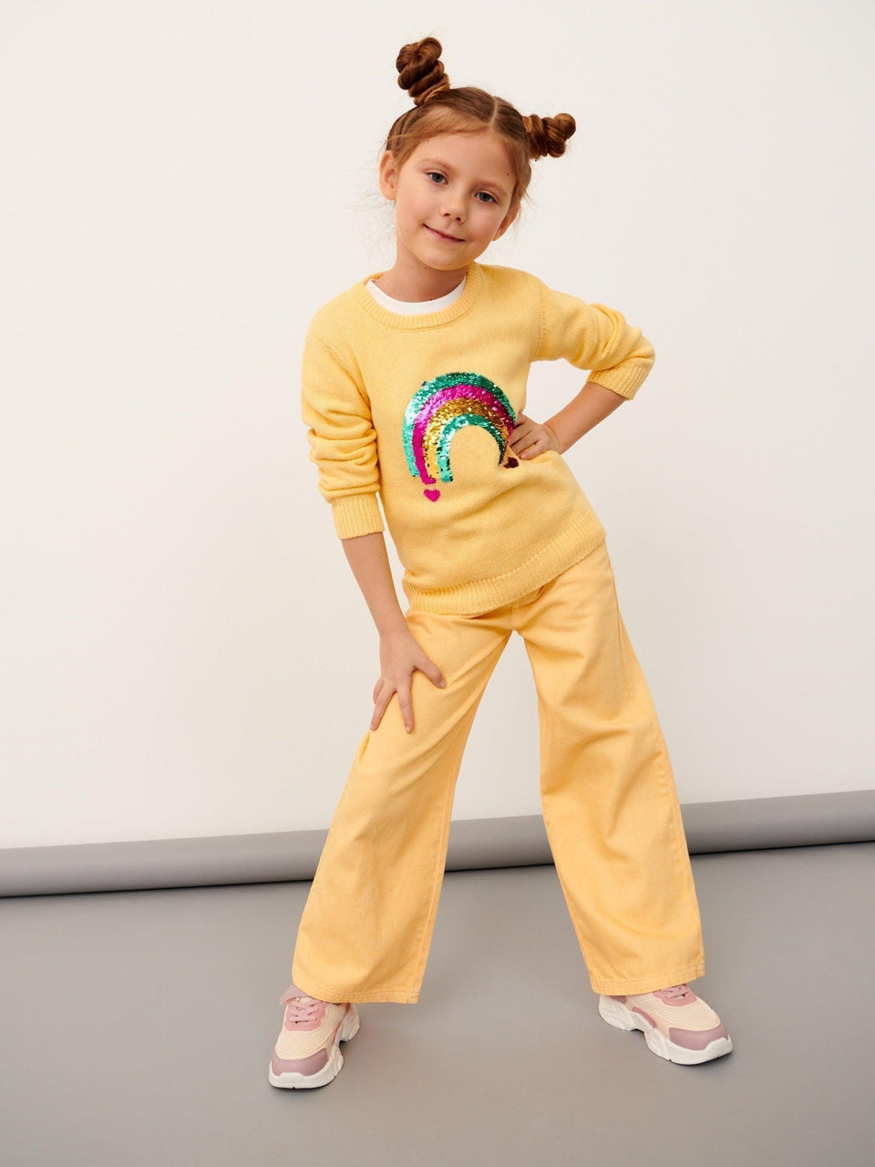 Child wearing a yellow outfit with a rainbow design on a plain background