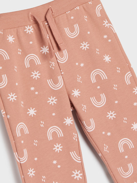 Pink sweatpants with white rainbow and sun pattern on a light gray background