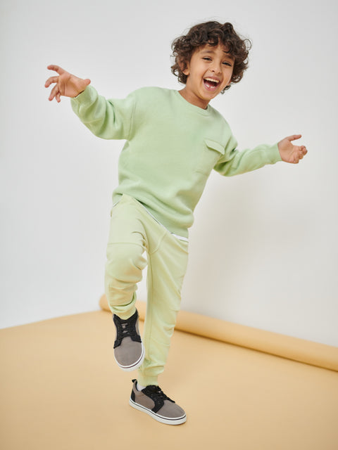 Child wearing a light green sweatshirt and pants on a beige floor with a white wall background