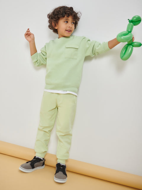 Child in light green outfit holding a green balloon animal against a white background