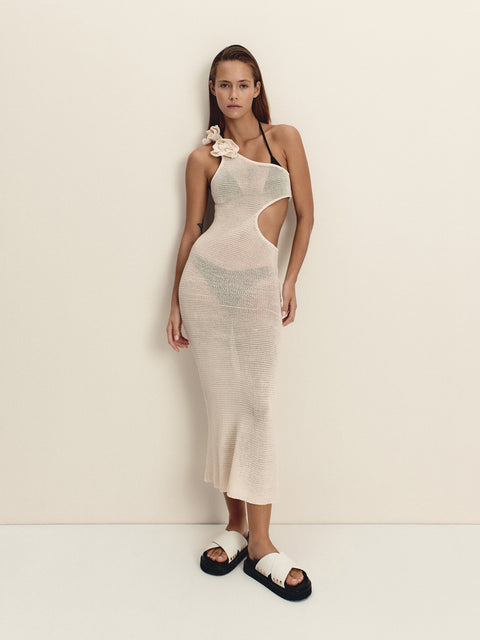 Woman wearing a beige one-shoulder dress with a slit, standing against a plain background.