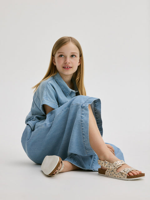 Young girl wearing a denim dress sitting on a light gray background