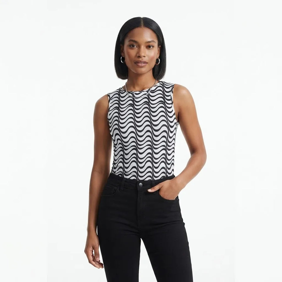 A woman modeling a sleeveless top with a black and white wavy stripe pattern, paired with black pants, against a plain white studio background.