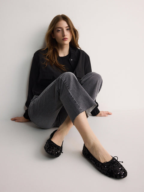 Woman wearing black sequin flats sitting on a white floor.