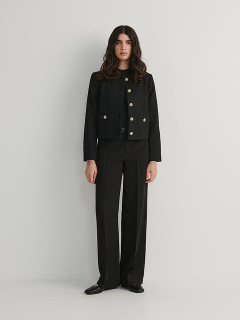 Woman wearing a black suit with gold buttons on a white background