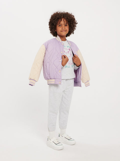 Child wearing a light purple quilted jacket with cream sleeves, white shirt, gray pants, and white sneakers on a white background.