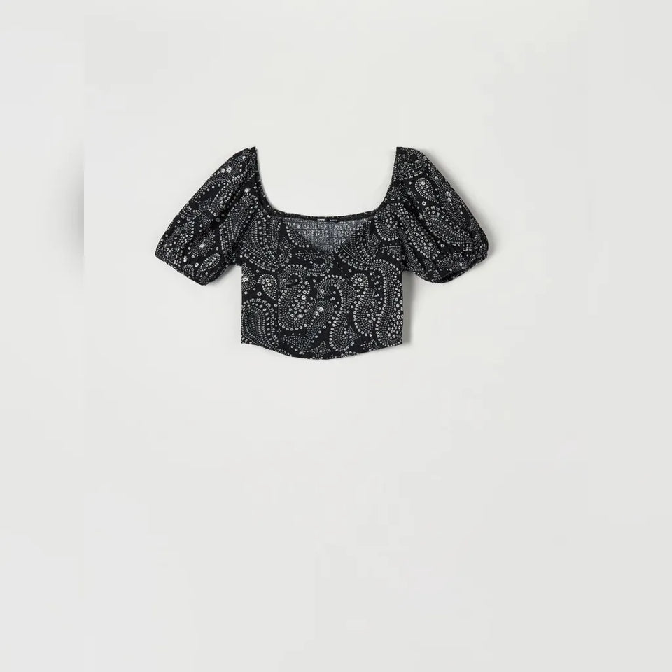 A black puff-sleeve crop top with a white paisley pattern, displayed flat against a light gray background.
