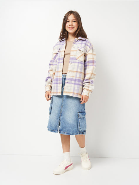 Person wearing a plaid shirt, denim skirt, and white sneakers on a white background