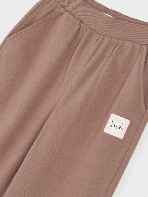 Brown sweatpants with a small white label featuring a cat design on a light gray background