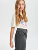 Young girl wearing a white t-shirt with colorful graphics and dark pants on a light gray background