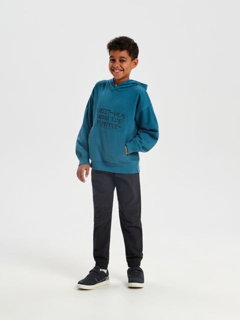 Child wearing a teal hoodie and black pants on a white background