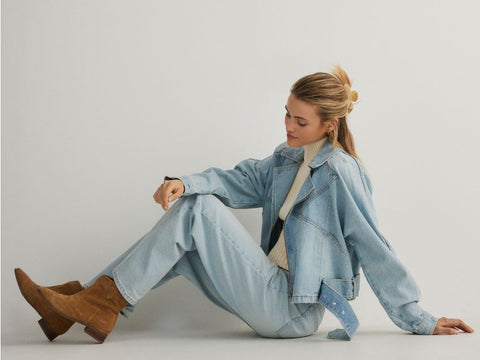 Person wearing a light blue denim outfit with brown boots against a white background