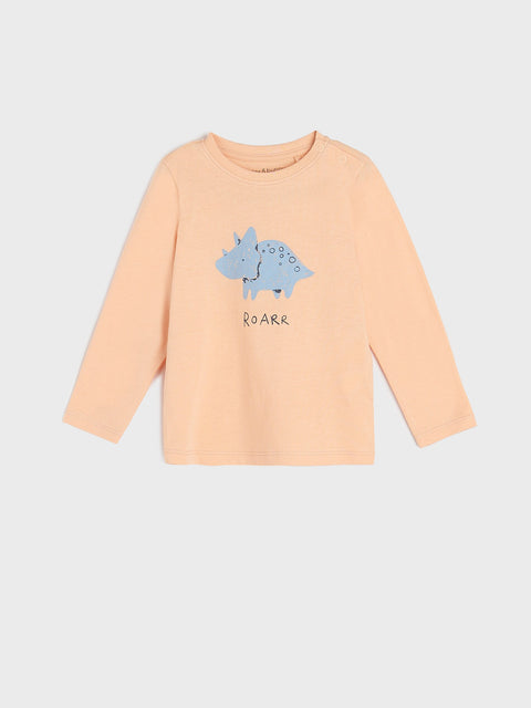 Peach-colored long-sleeve shirt with a blue dinosaur graphic and text on a light gray background
