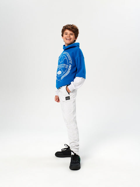Person wearing a blue hoodie and white pants on a white background
