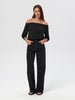 Woman wearing a black off-shoulder top and black pants on a white background