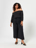 Woman wearing a black off-shoulder top and wide-leg pants on a white background