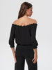 Woman wearing a black off-shoulder top and black pants on a white background