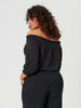 Woman wearing a black off-shoulder top and pants on a light gray background