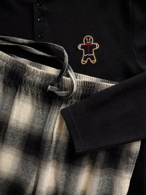 Black shirt with a gingerbread man embroidery detail on a plaid fabric background